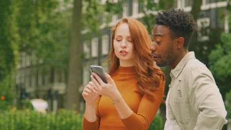 young couple travelling through city together following directions on map app on mobile phone