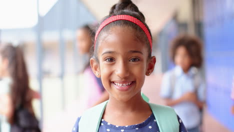 smiling girl with backpack standing in school hallway with classmates in background