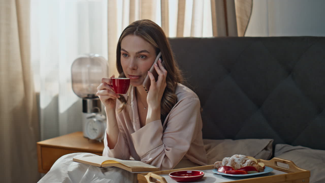 Donna che si gode la colazione a letto mentre parla al telefono