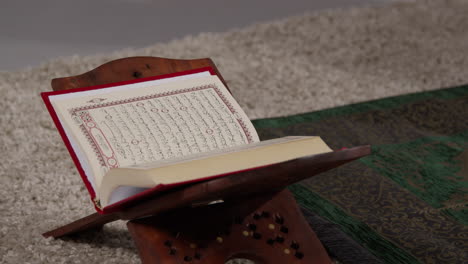 close up of open copy of the quran on stand next to prayer mat in muslim home