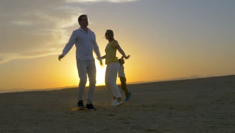 Glückliche-Dreiköpfige-Familie,-Die-Bei-Sonnenuntergang-Am-Strand-Tanzt