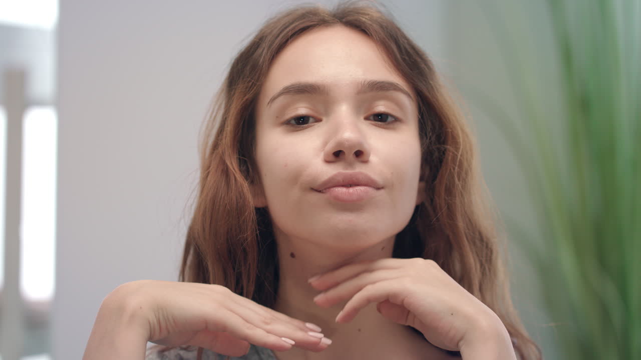 mujer joven haciendo masaje de piel en la cara y la barbilla espejo frontal en el baño