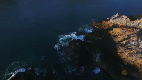 Drone-diving-down-fast-buzzing-a-rock-outcropping-to-reveal-a-serene-bay-with-two-small-sailing-yachts-anchored-near-the-shore