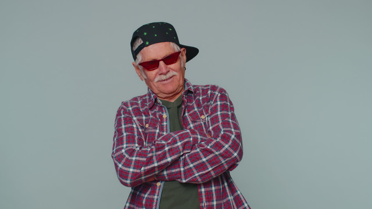 Seductive cheerful stylish senior old man in shirt wearing sunglasses, charming smile on pink wall