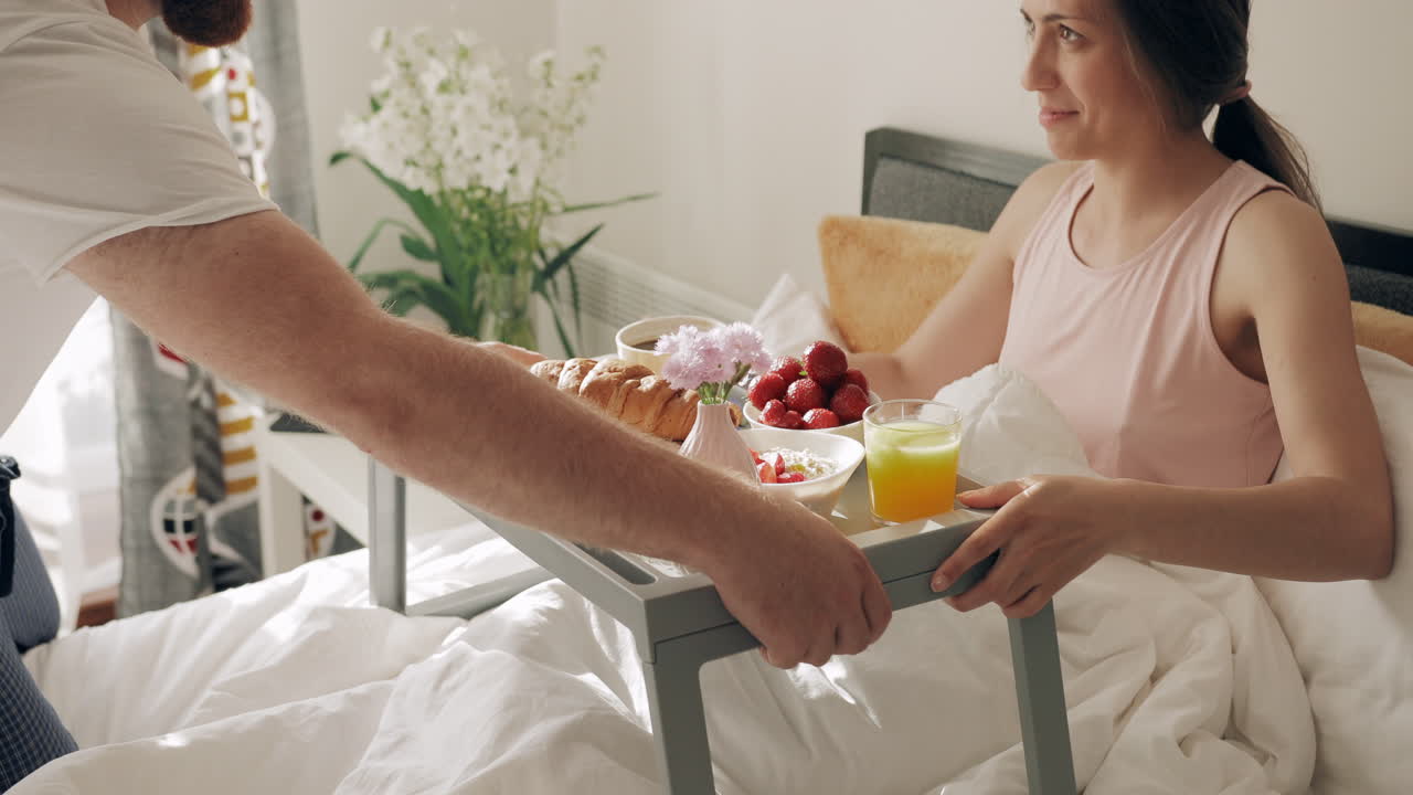 Un uomo serve una colazione romantica a letto a una donna felice