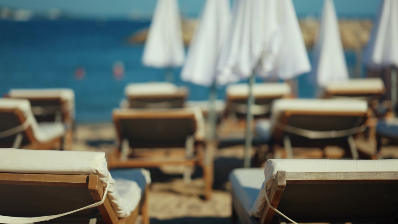 Detaillierte Nahaufnahme von ordentlich angeordneten hölzernen Sonnenliegen und weißen Kissen am Sandstrand.
