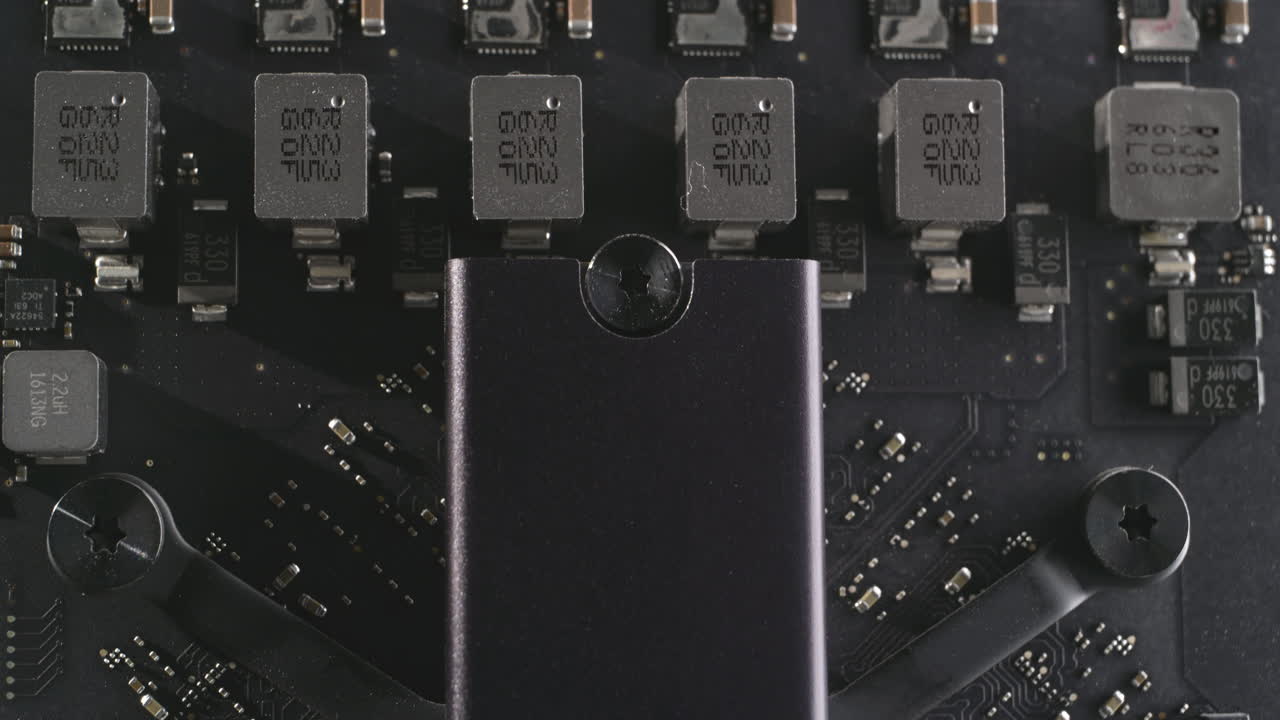 Macro shot inside a dark aluminium computer, highlighting SSD solid-state drive, motherboard, capacitors and components. Dramatic lighting, metallic, matten modern, reflective interior hardware