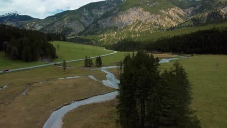 aerial flight along a scenic mountain river with fresh blue water in the bavarian austrian alps on a cloudy day, flowing down a riverbed along trees, rocks, forest and hills seen from above by drone