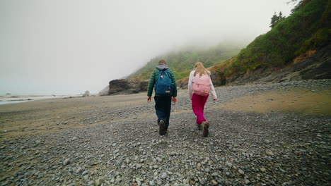 two people hiking on a misty, rocky beach along the coast