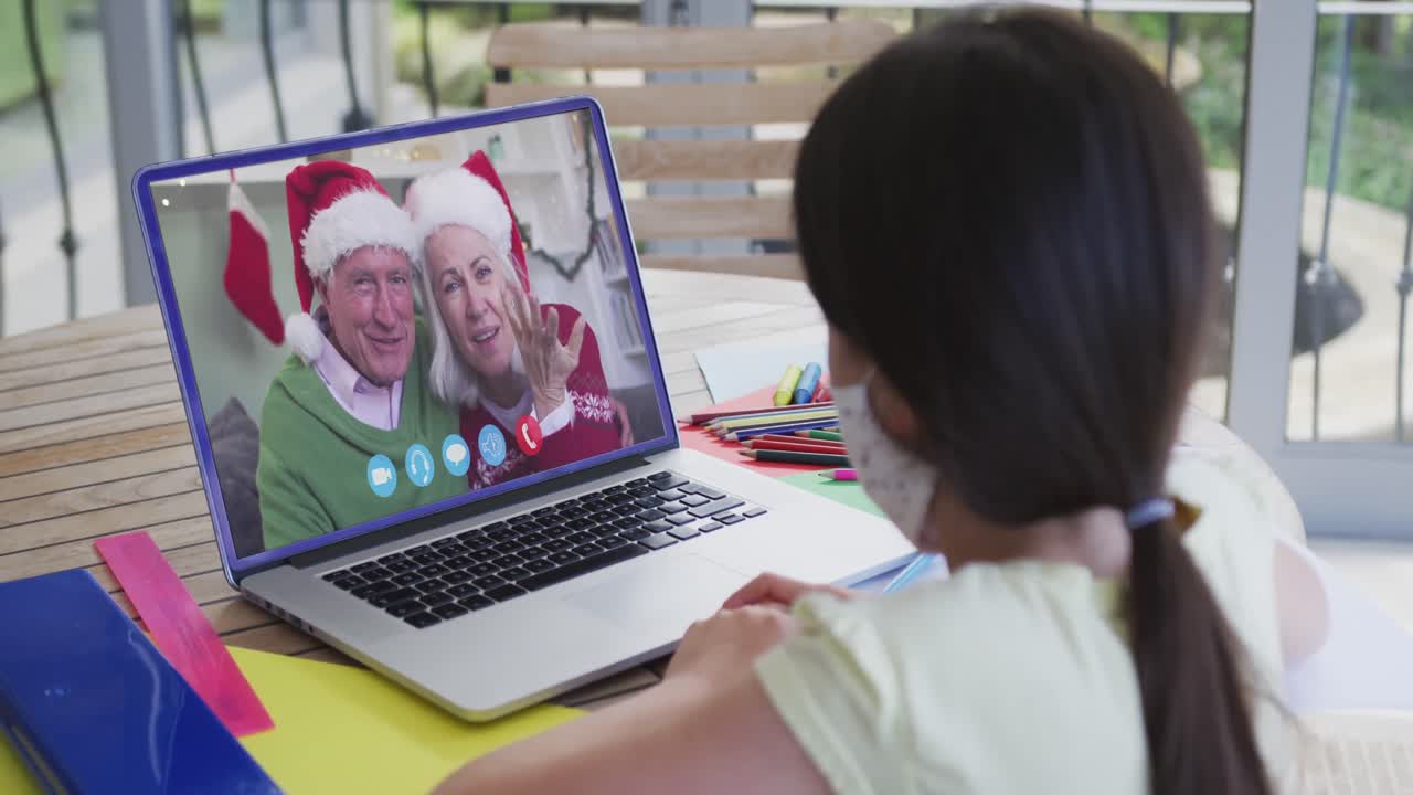 chica caucásica con máscara facial en la computadora portátil video chat durante la navidad en casa