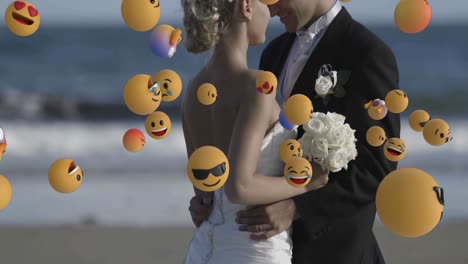 animation of emoji icons over happy caucasian married couple embracing at beach