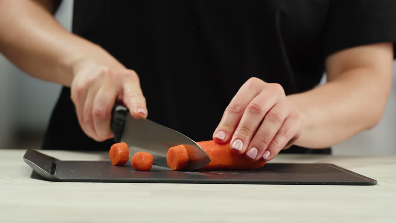Woman chef cutting carrot, with knife cuts fresh carrot slices for cooking. Cooking process on kitchen