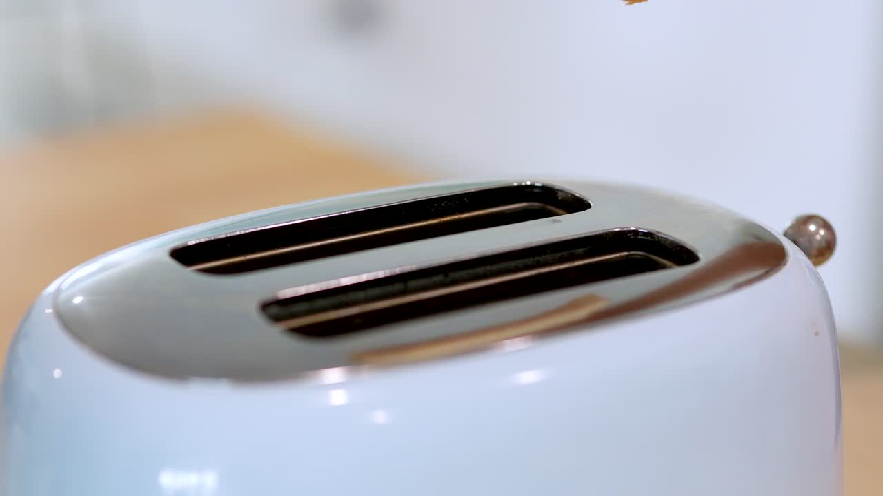 A person inserts two slices of white bread into a modern toaster on a kitchen counter, under bright, natural lighting with a shallow depth of field