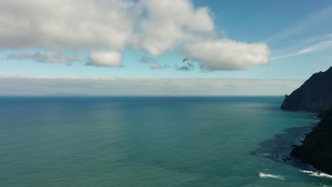 distant paraglider flies over open ocean close to shore of madeira, aerial