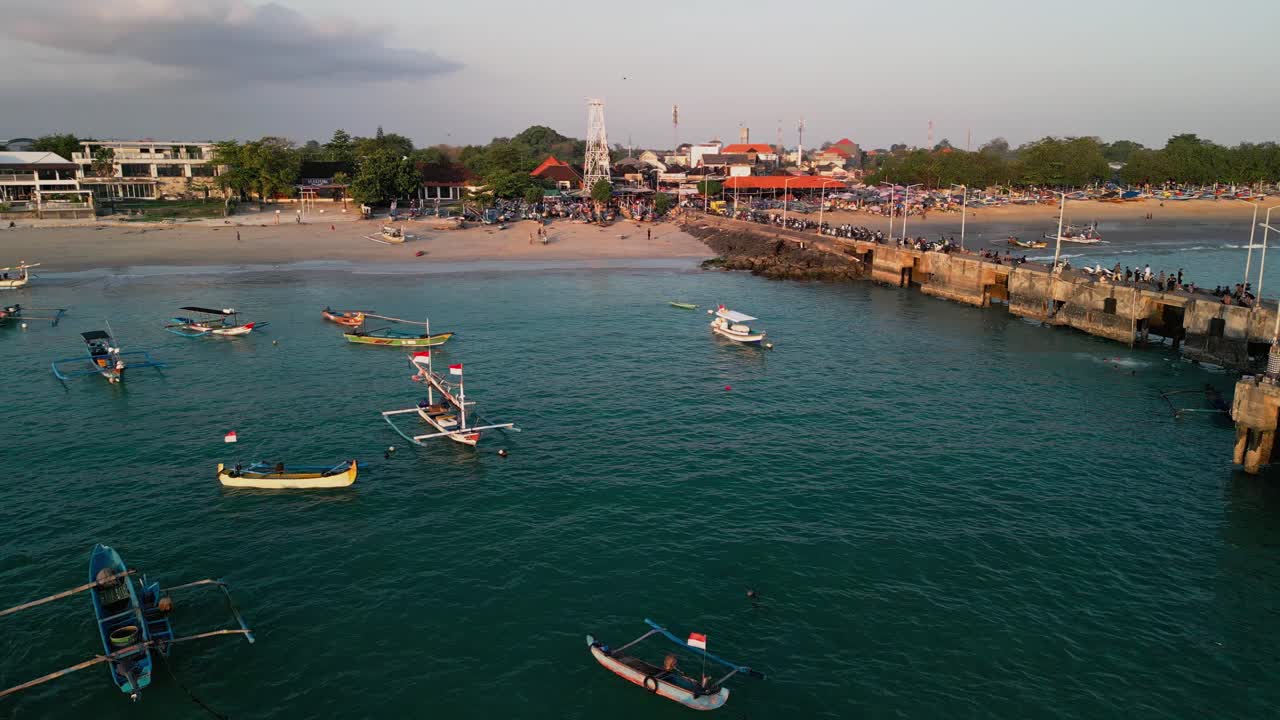 Aerial Bali fishing pier scene showcasing wooden boats on calm turquoise waters, coastal shoreline activity, and an authentic cultural atmosphere from a traditional island harbor