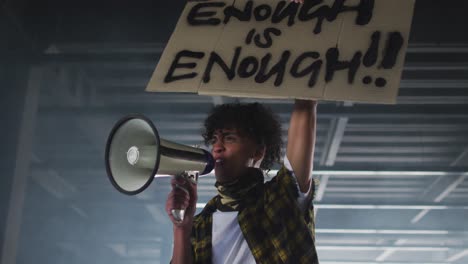 homme afro-américain portant un masque facial parlant dans un mégaphone tenant une pancarte de protestation dans un parking vide