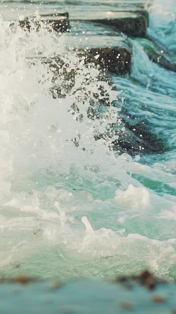 sea waves are crashing with foam on the rocks of the coast in the summer. Slow motion. Vertical video