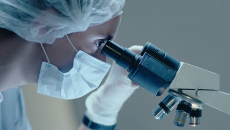 female scientist in mask and gloves looking in laboratory microscope