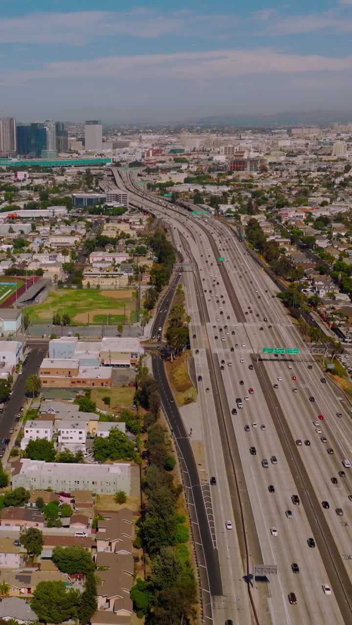 Multiple cars moving to and from financial downtown Los Angeles, California. Enormous urban territory of low buildings on sunny day. Vertical video