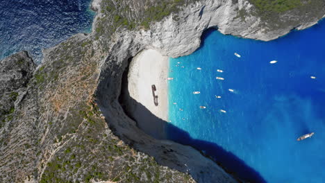 Aerial:-Rising-panoramic-top-down-view-of-Navagio-beach-on-Zakynthos-island,-Greece-during-summer