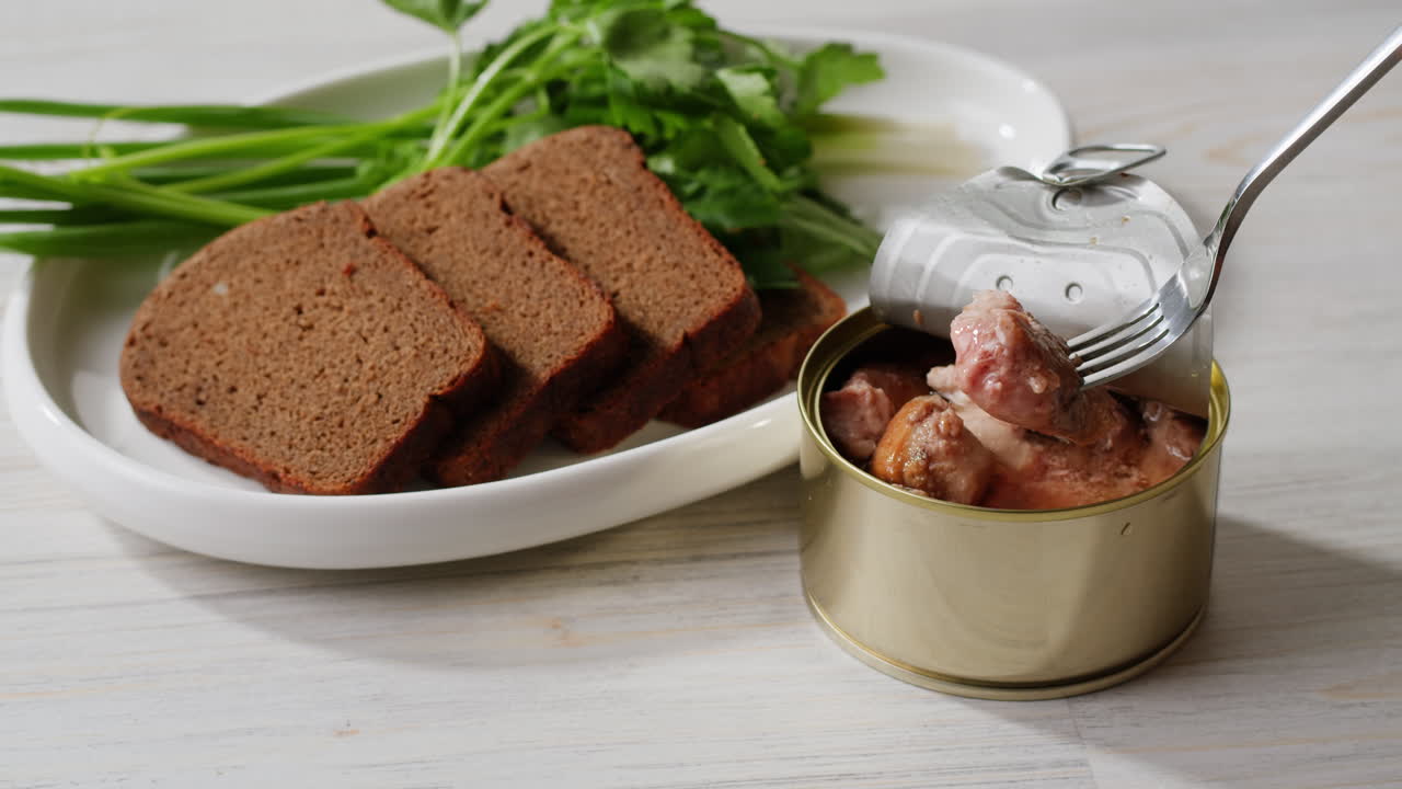 Smoked cod liver in oil in open tin can with fresh greens on wooden table. Seafoods delicacy. High quality 4k footage