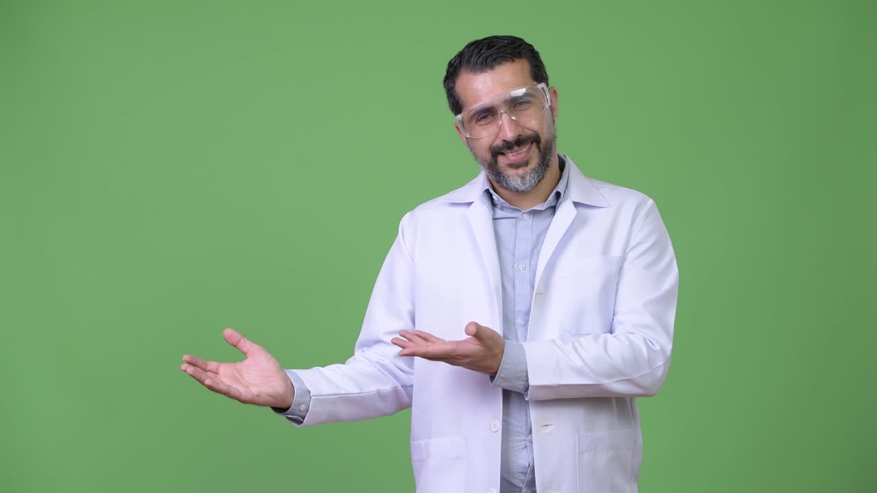 Medico persiano barbuto bello che indossa occhiali protettivi e mostra qualcosa