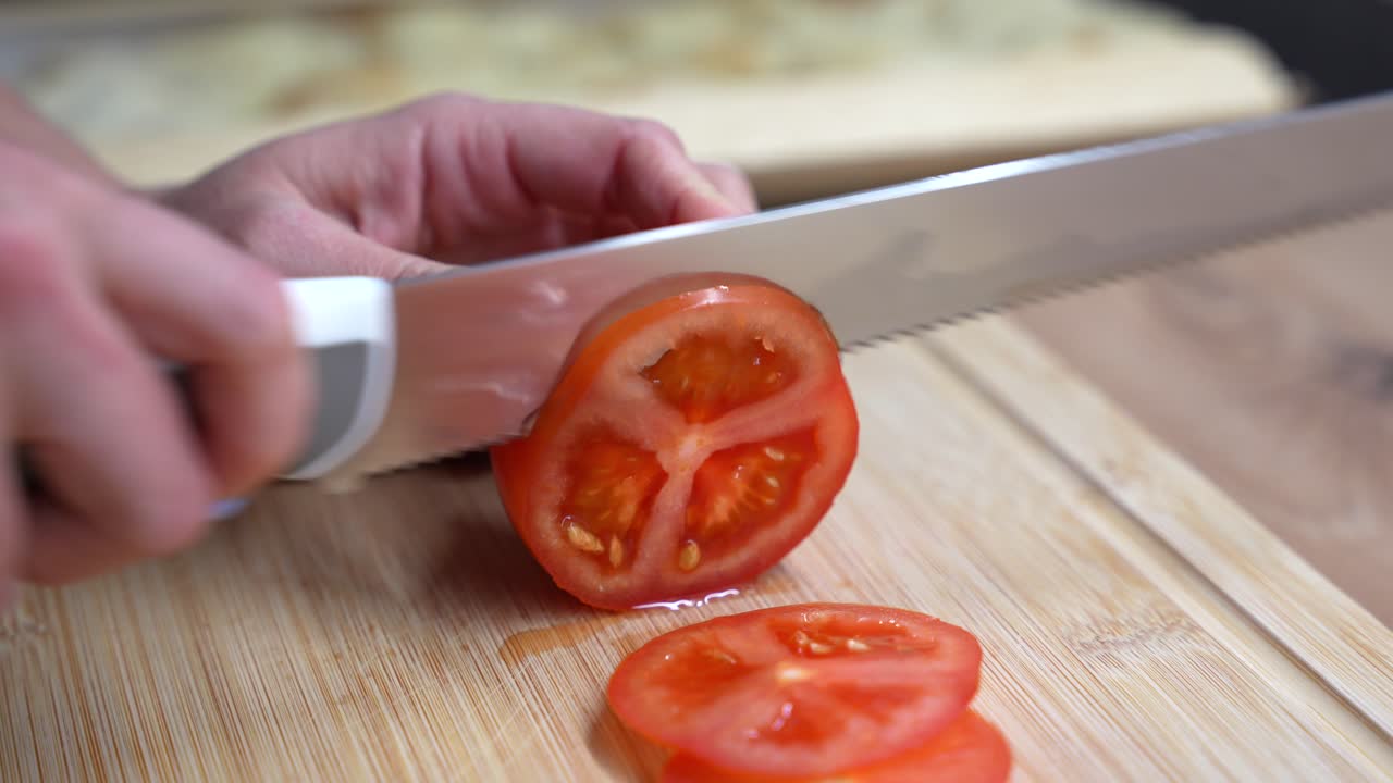 Close-up of female hands slicing a tomato with serrated knife