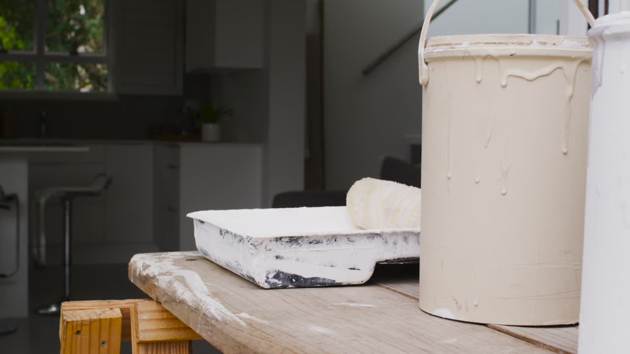 La telecamera esegue una panoramica lenta, rivelando una vaschetta per la pittura con rullo, due barattoli su un'asse e una finestra della cucina.