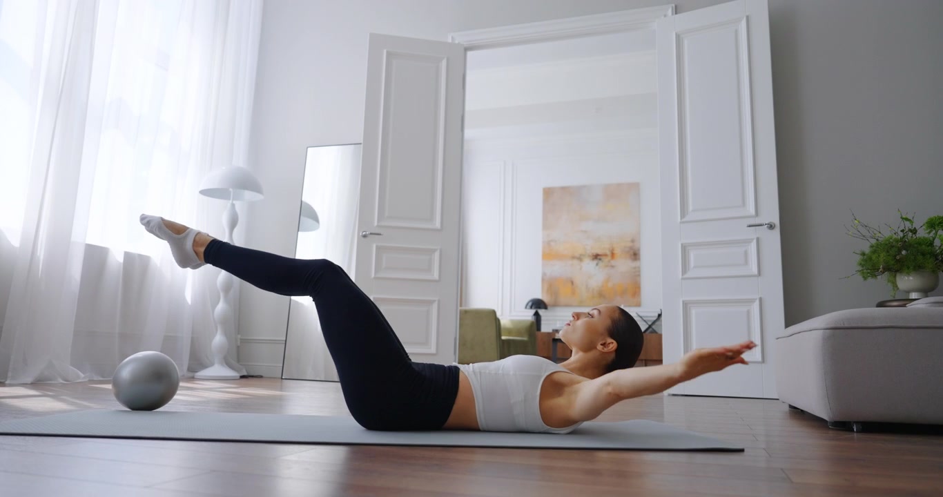 Giovane donna che esegue un esercizio Pilates per il core su tappetino a casa
