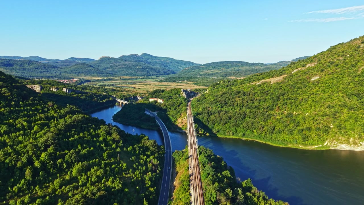 View of hills and water with railroad tracks running along the river in the countryside during daytime