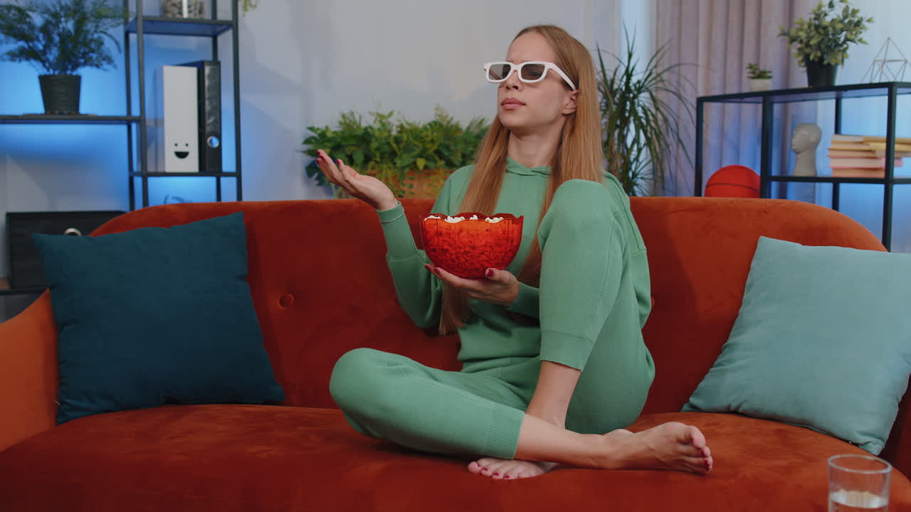 chica sentada en el sofá comiendo palomitas de maíz y viendo interesantes series de televisión, juegos deportivos en línea en casa