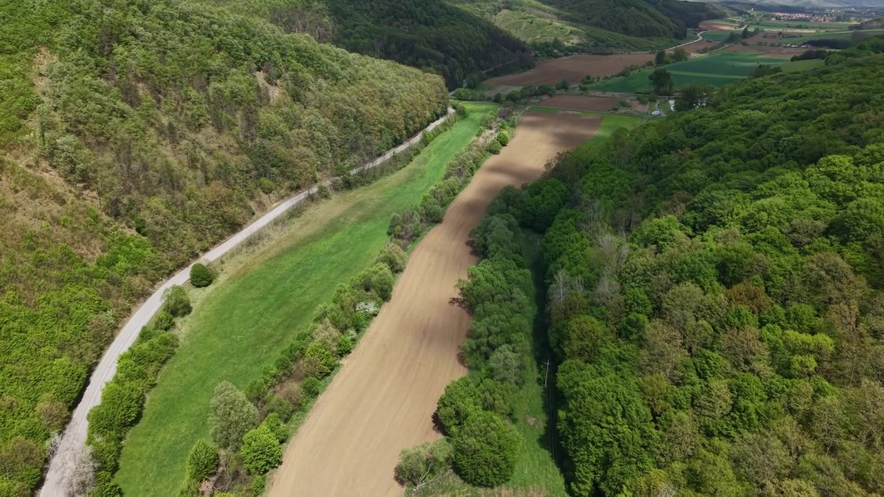 Una prospettiva aerea da drone di una stretta strada tortuosa che attraversa campi verdi e fitte foreste in campagna.