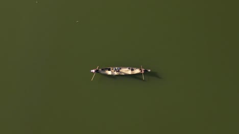 top-down aerial shot of a small wooden boat in a lake with fishermen on board catching fish using fishing net