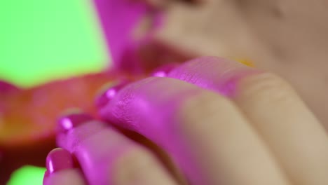 woman biting into a juicy orange slice, green background, neon purple lights