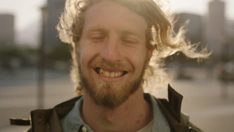 portrait of handsome bearded hipster man smiling happy at camera wind blowing hair in urban city background