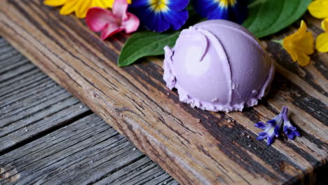 scoop of purple ice cream or sorbet with colorful flowers on a wooden board