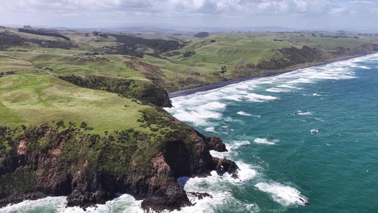Ripresa aerea con drone in allontanamento di verdi scogliere costiere, spiaggia di sabbia nera e onde turchesi dell'oceano, Nuova Zelanda, vista paesaggistica epica.