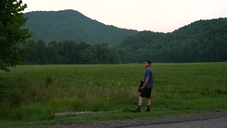 a wildlife photographer with a long telephoto lens looking for birds in the backdrop of a meadow and forested mountains