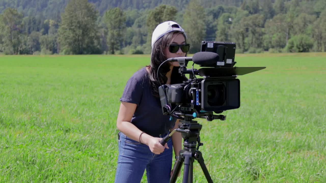 Woman operating a cinema camera on an open field