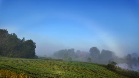 foggy countryside field with soft morning light and a rainbow over misty trees and farmland