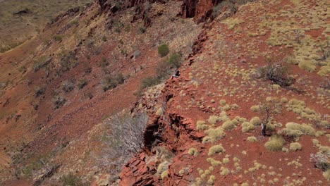 Man-sitting-on-the-edge-of-desert-mountain-in-Western-Australia-and-enjoying-view-during-sunny-day---Aerial-orbiting-shot