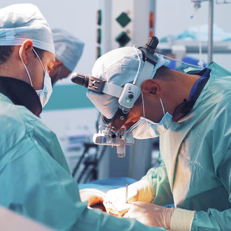 surgeon with magnifying glass on his head is working with assistants in operation room. team of specialists in medical uniform performing an operation to a patient with special instruments in clinic.