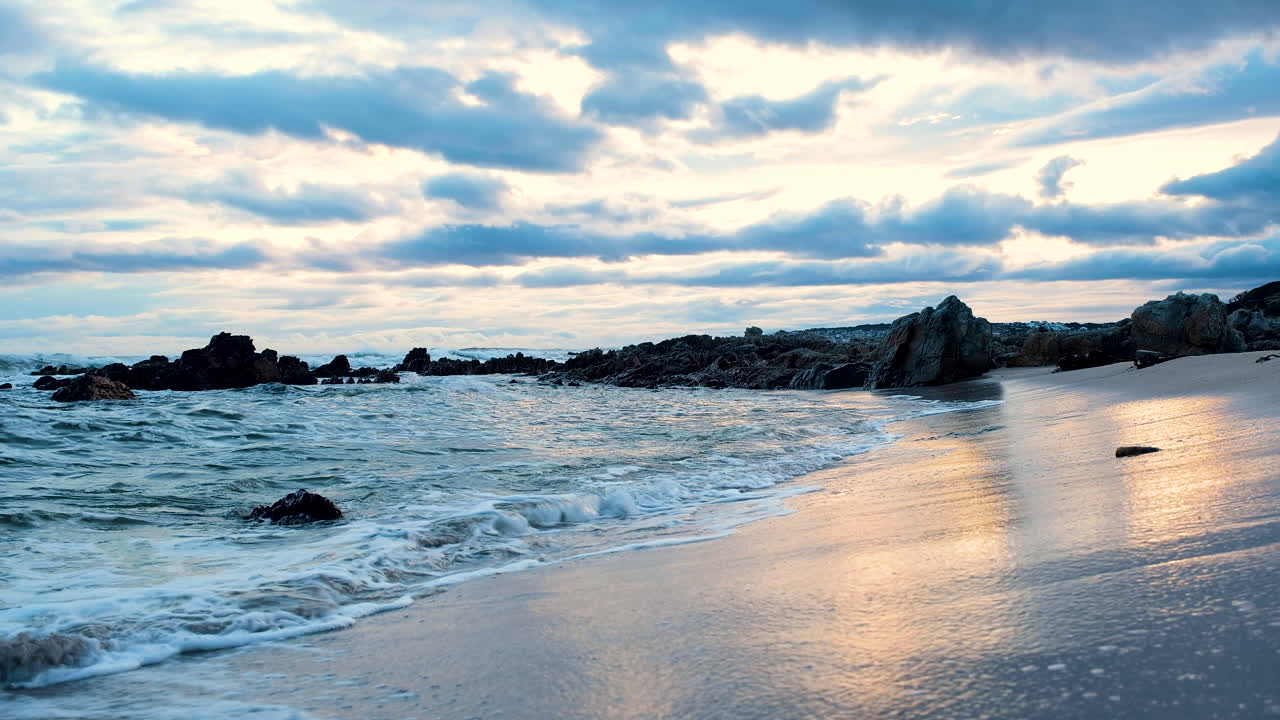 vista tranquilizadora de las olas rompiendo en la playa, disparo de levantamiento revela nubes de atardecer de mal humor