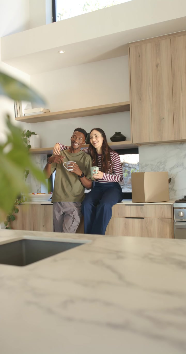 Video vertical: Pareja diversa posando en la cocina, el hombre extendiendo el teléfono para una selfie, sosteniendo tazas y una caja.