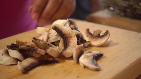 hands slicing white mushrooms on a cutting board