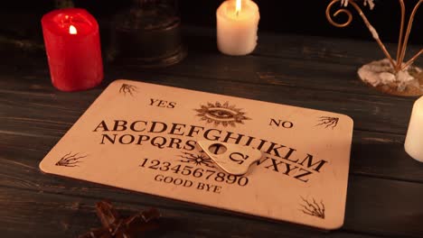 close up video of a wooden ouija board on a table surrounded by candles and a cross in a muffed - close up video of a wooden ouija board on a table. wax candles and a cross around. the planchette is slowly moving across the board, spelling out words and numbers. creative mystical content