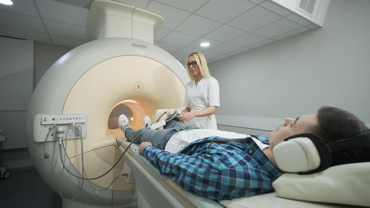 mujer médico hace escaneo de resonancia magnética de la articulación de la rodilla. joven paciente en la mesa automática entra en una máquina de resonancia eléctrica de tipo cerrado usando auriculares de aislamiento de ruido. equipo moderno, bobina en la rodilla del paciente