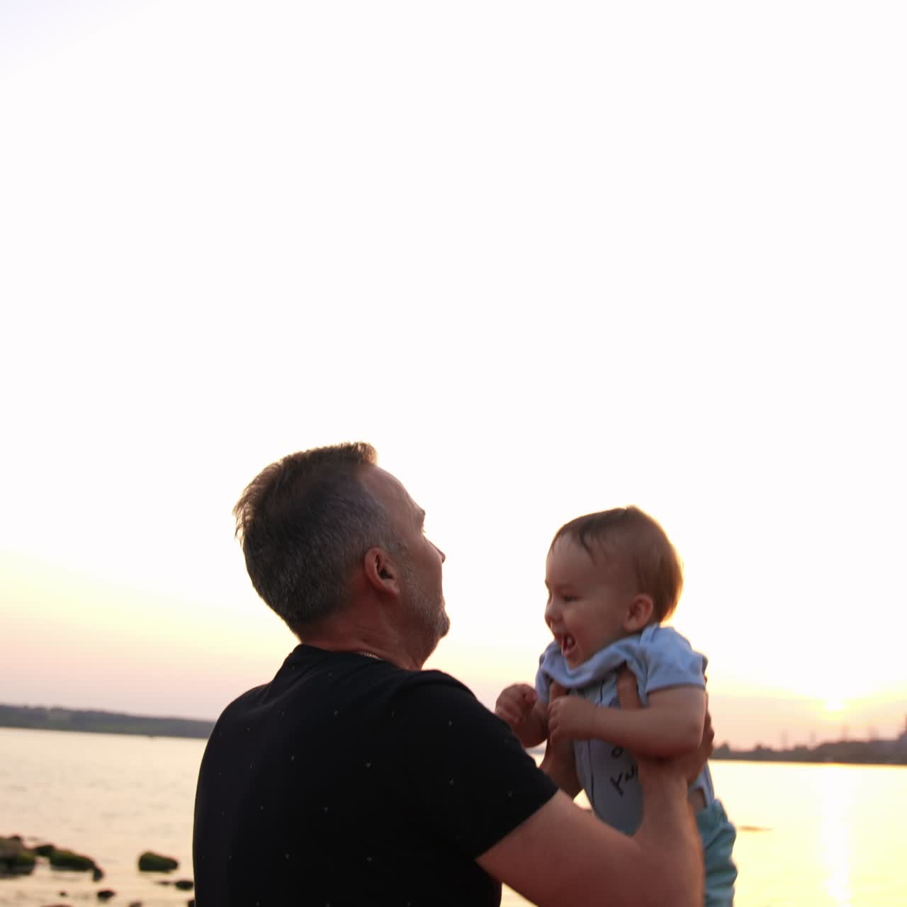 Tempo prezioso trascorso in famiglia nella natura. Papà affettuoso che gioca con il suo figlioletto lanciandolo in aria e prendendolo. Fiume sullo sfondo