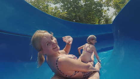 una familia feliz con un niño está montando un tobogán de agua riendo agitando sus manos a la cámara lenta m