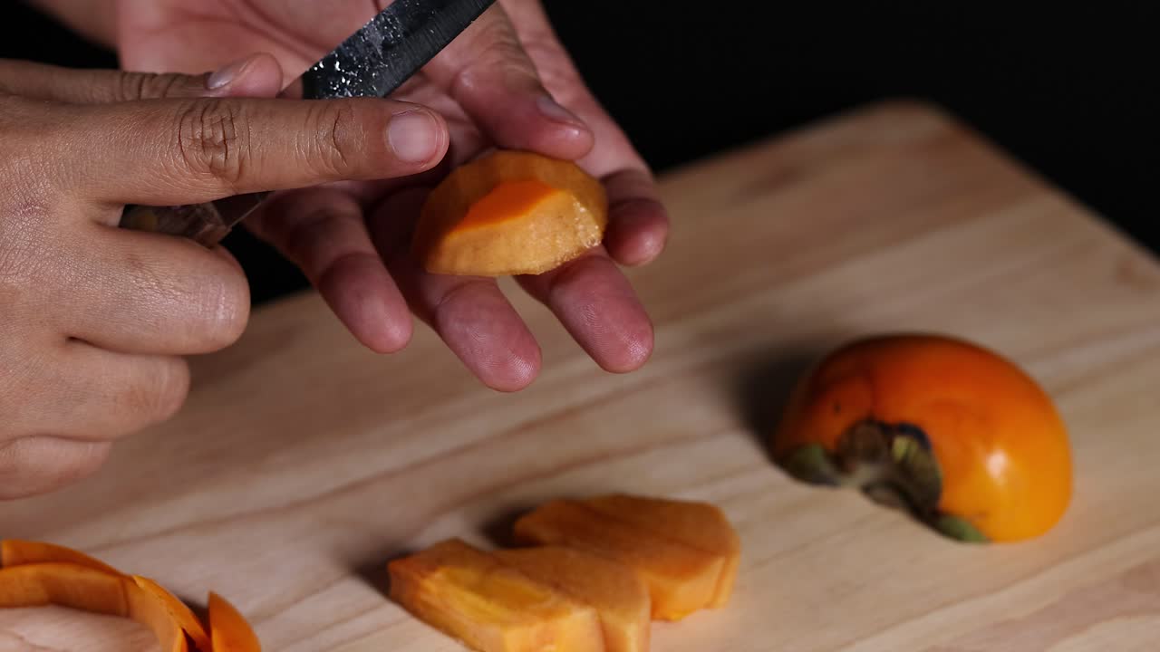 Hænder skærer persimmon med en kniv.